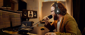 A professional music producer wearing Talomen Ti660x Professional Studio Monitoring Wired Headphones while recording vocals in a studio, surrounded by high-end audio equipment.